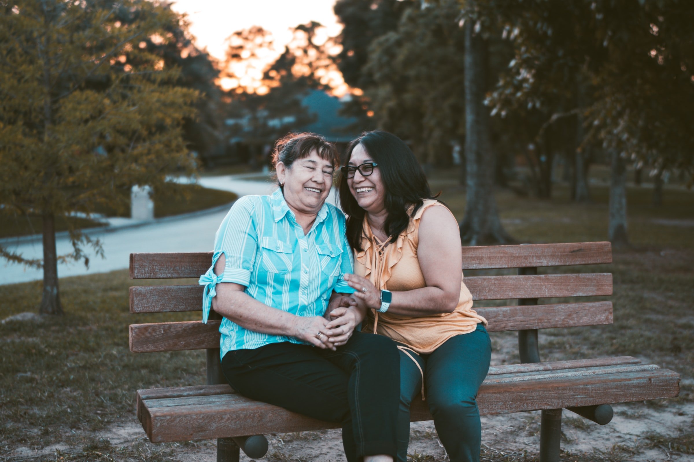 A picture of two women, sitting on a park bench, in dialogue, smiling.