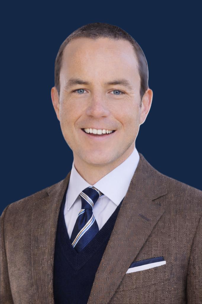 Edward Mooney, GCSE English author and tutor, wearing a brown tweed jacket and navy tie, smiling against a light background.